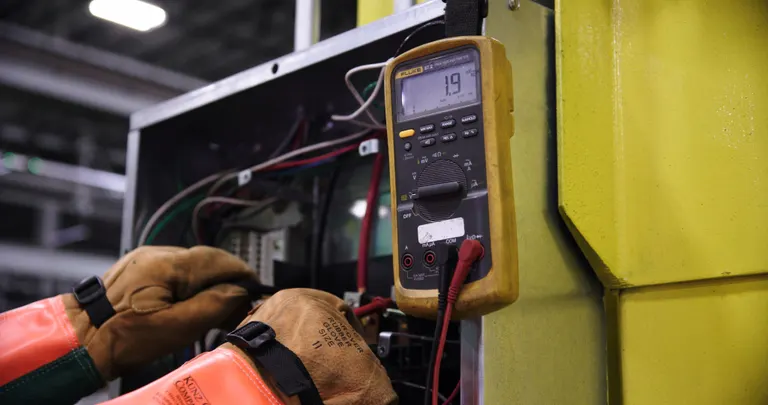 Elektryk z multimetrem podczas pomiarów w szafie sterowniczej